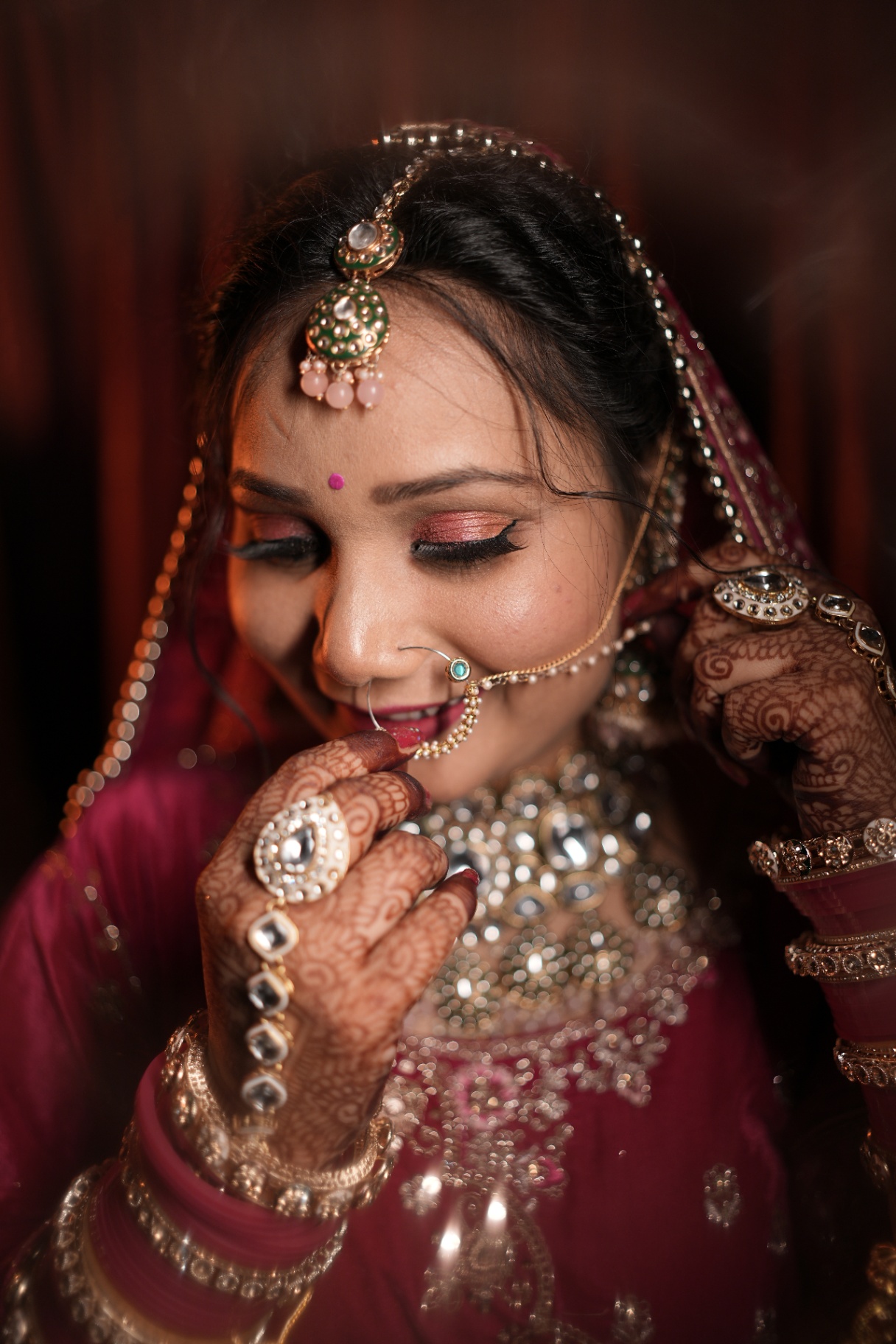 Close portrait of Sakshi adjusting her nath, kundan jewellery catching the warm light of the room