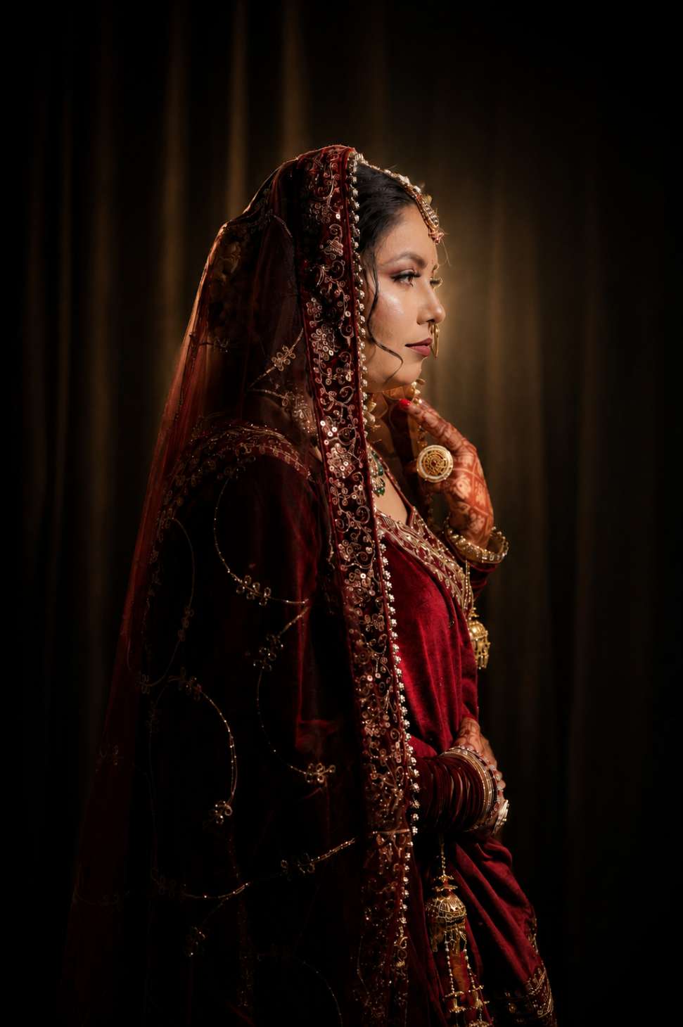 Studio profile — Renu in maroon velvet against a warm halo of light, a single quiet frame