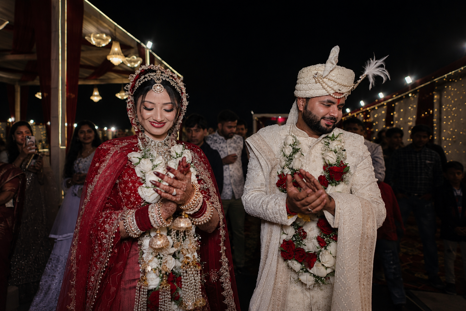 Couple in bridal attire exchanging garlands under warm ceremony lights