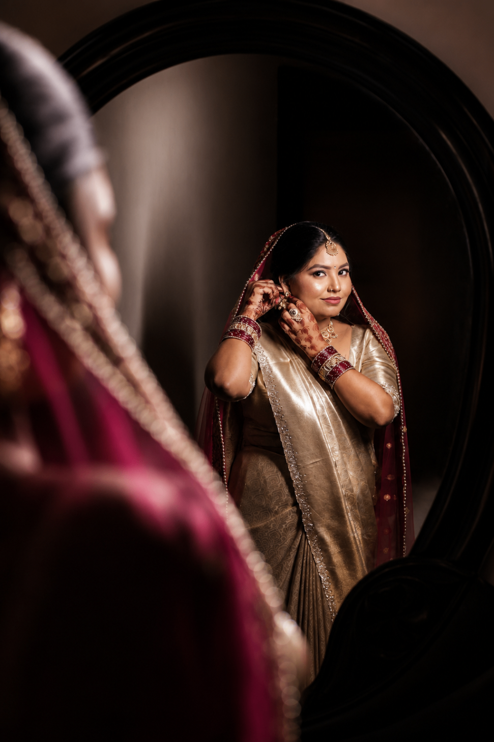 Getting-ready room — Renu at the round mirror in gold silk, adjusting an earring in Lucknow morning light