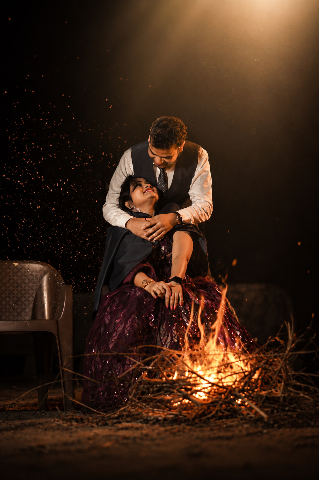 Sarita laughing in a maroon gown as Dharmendra holds her by a bonfire under a spotlight