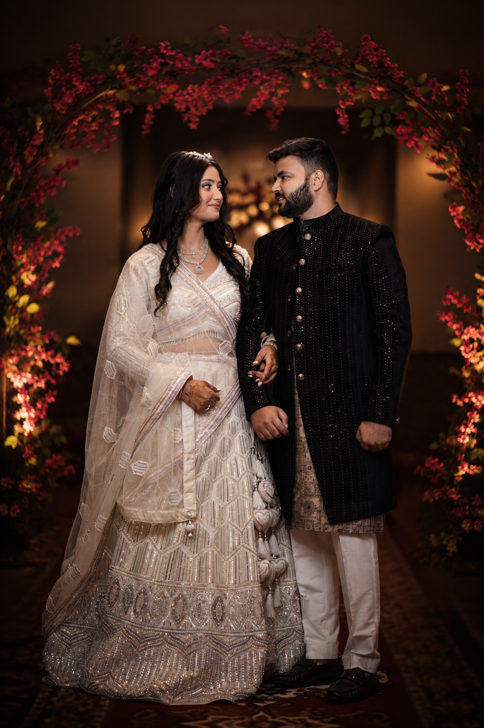 Sangeet night — Vaishnavi in ivory and Abishek in black, framed by a bougainvillea arch