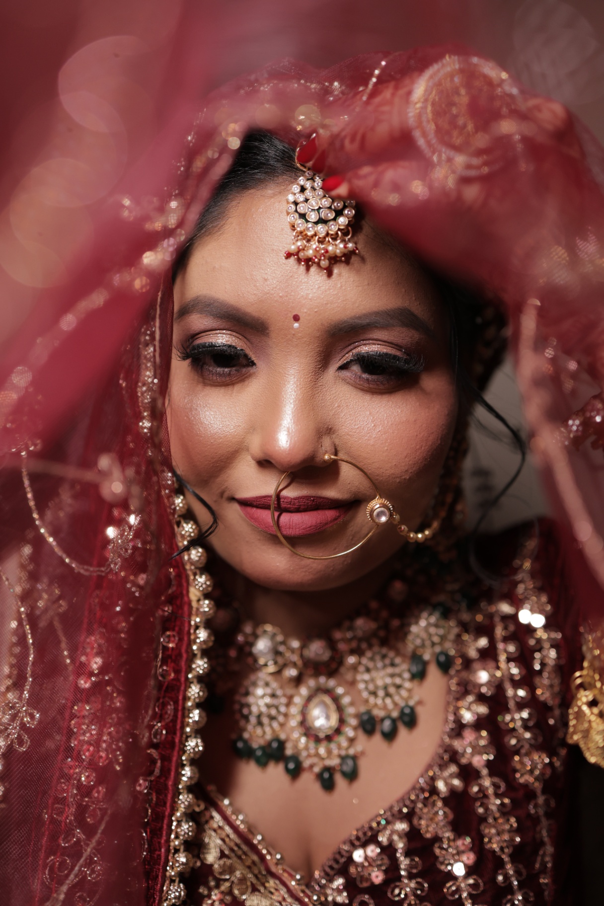 Formal portrait of the bride draped in crimson, pearls of the maang tikka on her forehead
