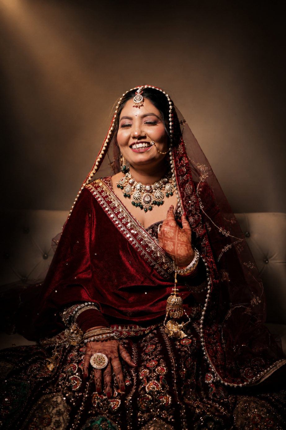 The unguarded laugh — Renu seated in maroon velvet, eyes closed, kundan resting on her collar